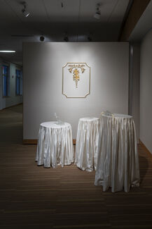 Art installation by Kitty Rauth depicting three clothed tables and an artwork suspended on the wall in a gallery space 