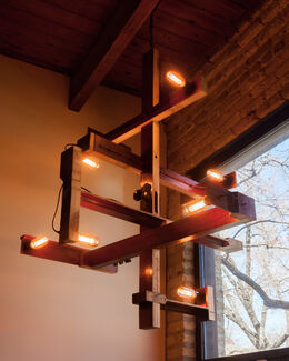 Light and wood sculpture by Laura Miracle suspended from the ceiling of an indoor space.