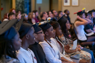 A group of CAAP students sit while wearing graduation caps, looking toward the front of the room.