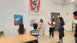 A group of five students stand looking at artwork on a wall.