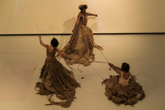 Three people wearing sculpted skirts and holding a rope to form a triangle.