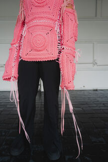 A person models a pink, handwoven sweater with intricate details and pink ribbons. 