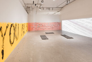 Gallery space installation by Bri Beck of text reading "YOU ARE SO positive" in varying styles wraps three walls against colorful backgrounds.