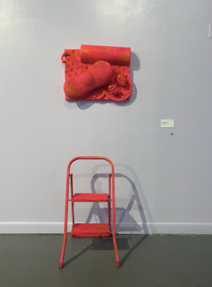 An orange scale sculpture by Bri Beck of various found objects, including a step ladder and back massager. 