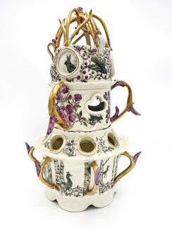A white ceramic piece with three tiers, gold handles, and purple flowers.