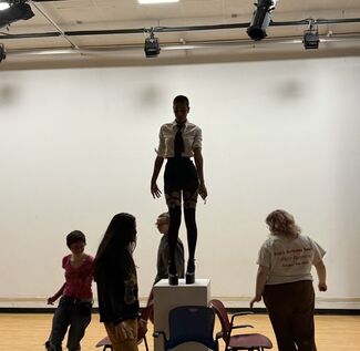 Morgan stands on a pedestal in the 012 space, while students walk around them in a circle. 