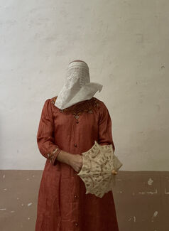 A person standing in a red dress with a white face covering.
