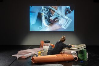 A person painting a glass plank with a white substance is projected on the wall in front of them. 
