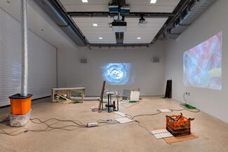 Projected images and objects such as crates, storage boxes and aluminum tubes displayed in a gallery space. 