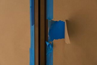 Peeled brown paper revealing blue underneath with blue painter's tape bordering the paper. 