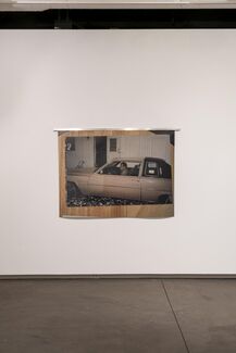 A photograph of a man in a car is mounted to a wall in a gallery space. 