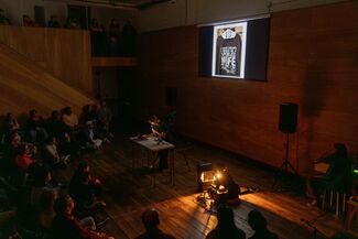 Camille Johnson performs to an audience holding a microphone and standing in front of a projection of a graphic t-shirt. 