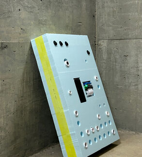 A light blue and neon green foam board with holes leaning against a wall. 