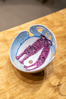 Pink and blue painting inside of an eggshell by Emily Miller depicted a mirrored cat stretching. 