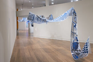 A blue and white and gray print on film suspended from the air in a gallery setting.