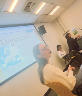 Three people in a classroom with a slideshow being presented. 