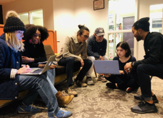 Students of varying ethnicities, ages, and genders work on two laptops. 
