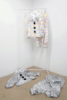Clown garb hanging on a rack and draped on the floor in a gallery space. 