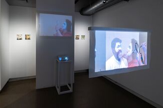 Projections in a gallery space of people applying clown makeup.