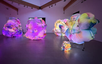 Colorful inflatable art installations lit up in purple light inside a dark gallery setting.