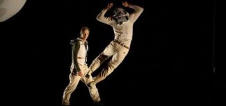 One adult jumping in the air while another adult stands in the background. 