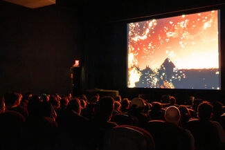 An audience in a theater watching a projection of an orange, yellow, and black image.