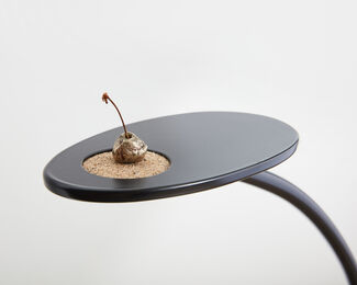 A bronze cherry in a small circular pit of sand on a black surface. 