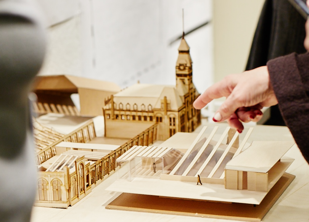 A person points at details of a wooden laser cut architectural model.