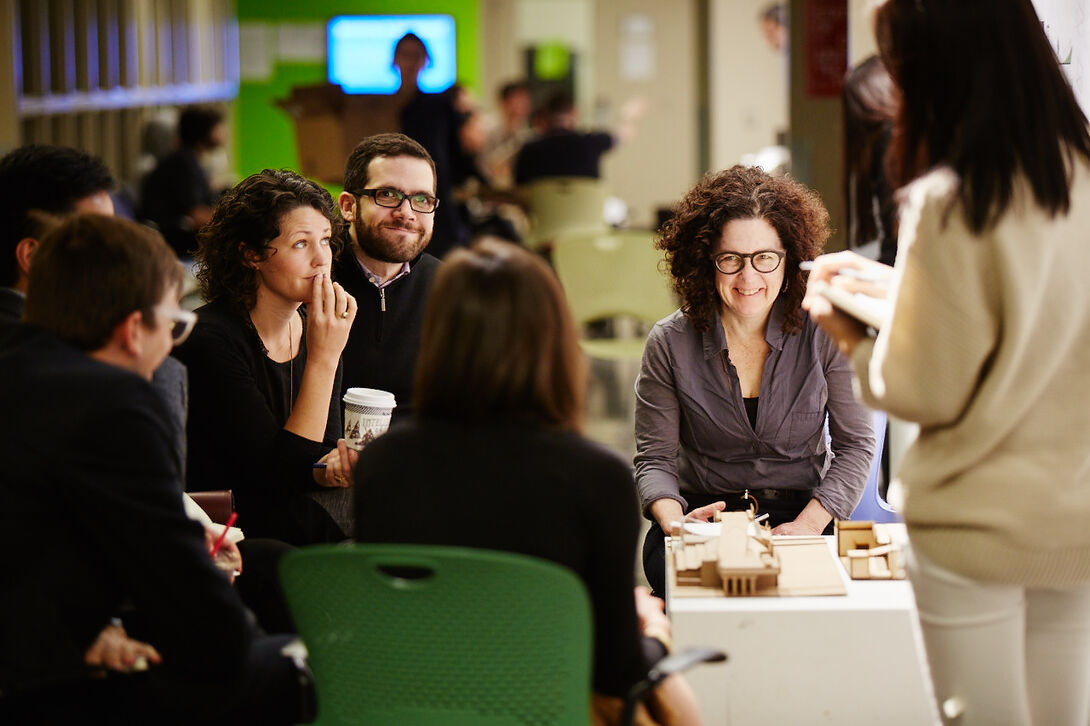 A group of people sitting and talking in front of an architectural model.