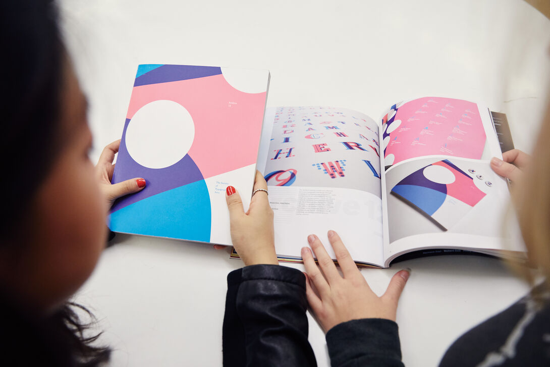 Two people looking at a purple, pink and blue booklet. 