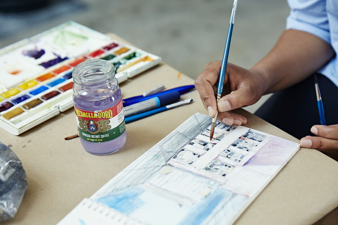 A detailed shot of a person using watercolors to paint a picture in a sketchbook. 