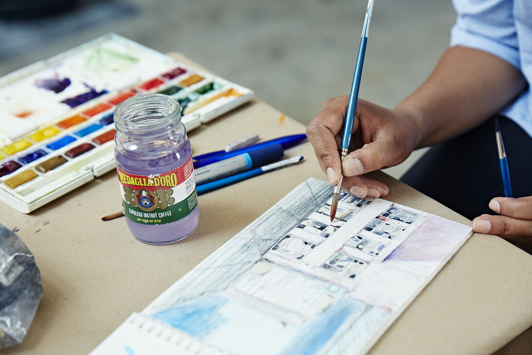 A detailed shot of a person using watercolors to paint a picture in a sketchbook.
