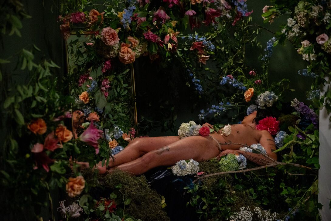 Ale Campos, dressed as Celeste, in repose surrounded by flowers