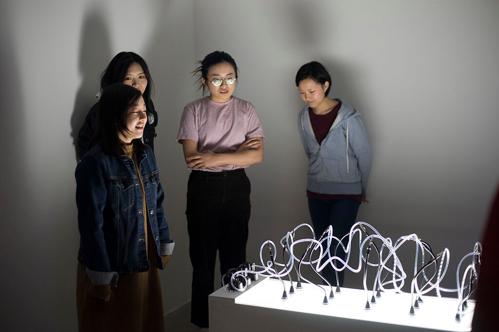 Three students stand around a light installation