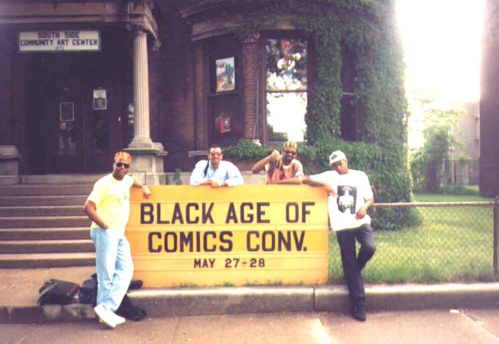 Four people gather around a Black Age of Comics Convention sign