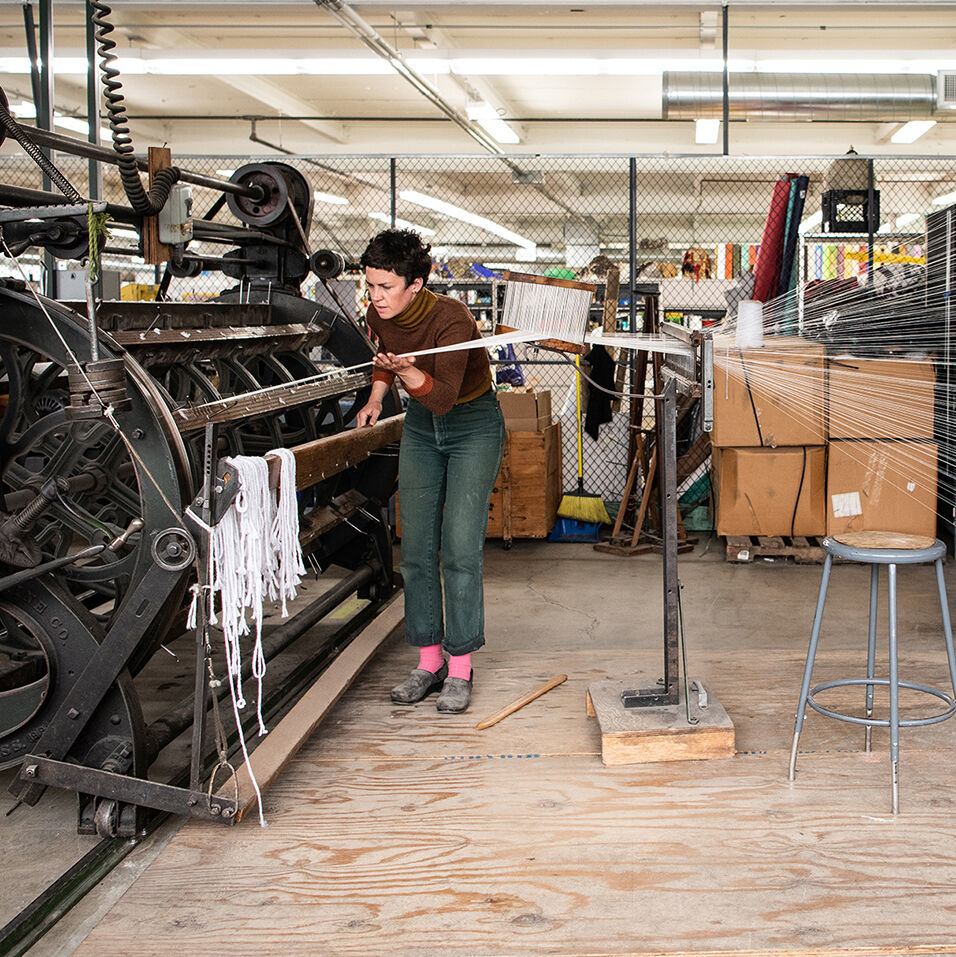 Studio shot of Emily Winter in the process of warping an industrial loom.