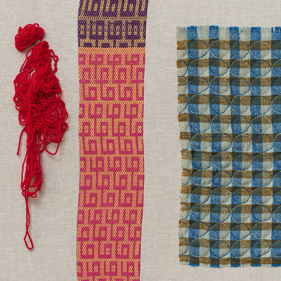 Detail image of two colorful, woven patterns stitched to a cream colored background alongside tangled, red yarn.