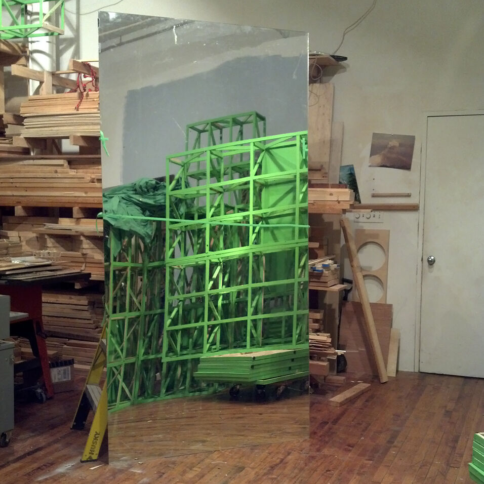 A green grid is reflected in a mirror against the backdrop of the artist's studio.