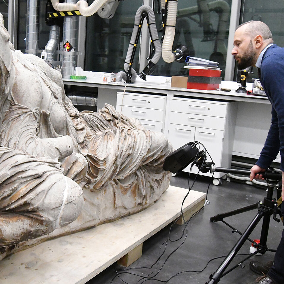 A marble statue in a lab-like setting is examined by Giovanni Verri.