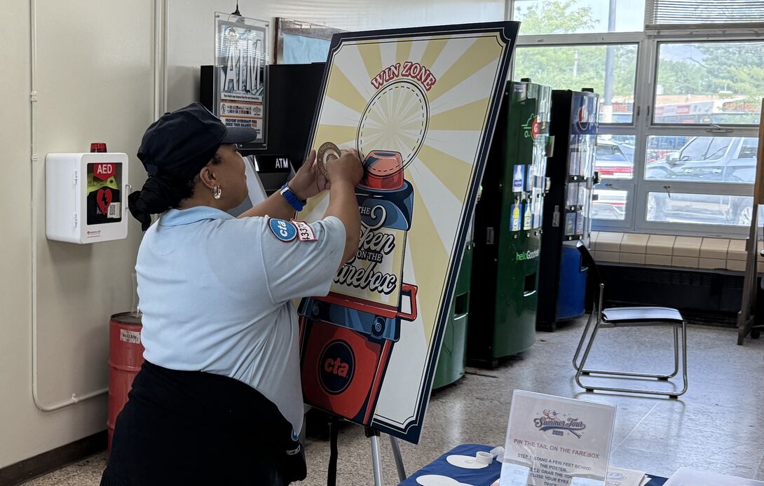 A CTA employee prepares the “Pin the Token in the Fare Box” game board that Nickels designed for an employee event