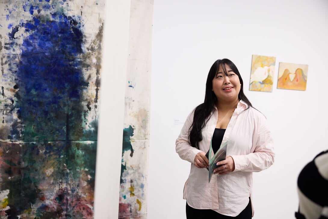 A person standing next to hanging artworks at an exhibition. 