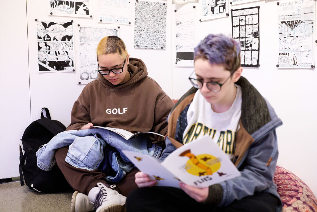 Two students viewing booklets from an exhibition. 
