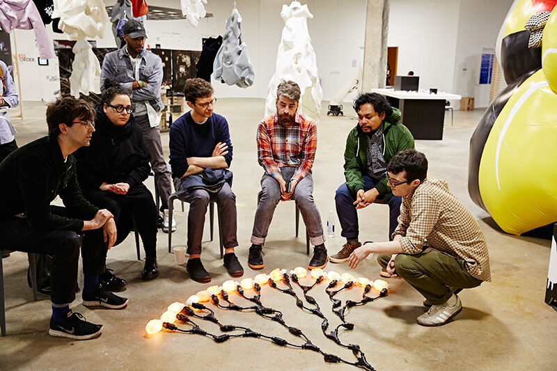 Group of students looking at illuminated light bulbs on the floor at art installation.