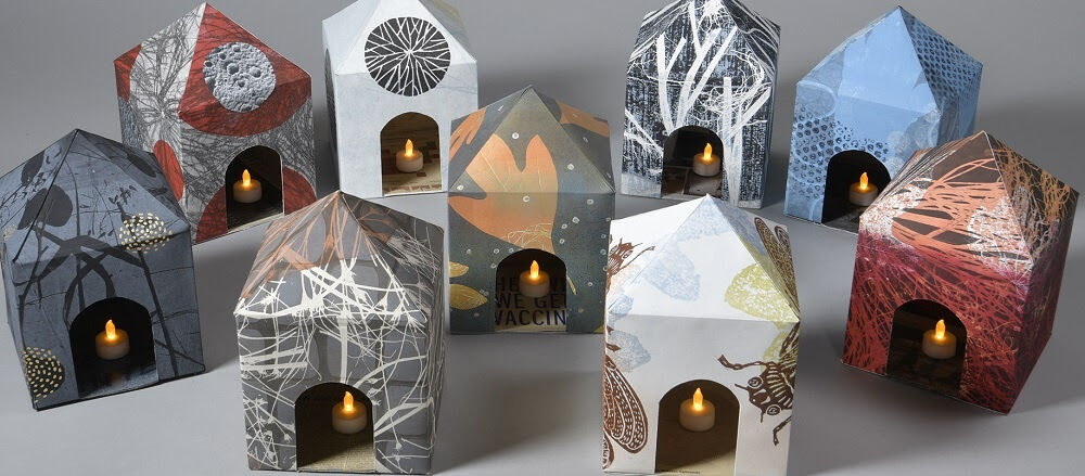 Small houses made out of patterned paper holding candles