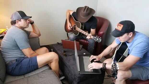 Three men sit at couches and compose a song on the guitar