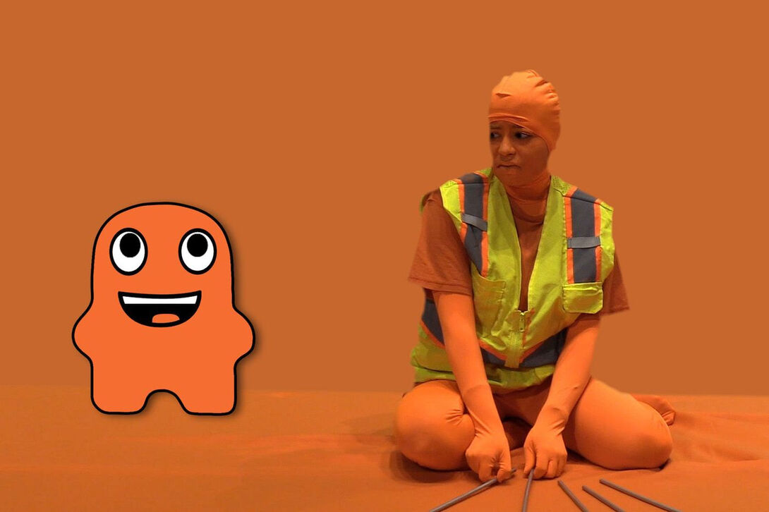 A woman sits in an orange room wearing a safety vest with a cartoon orange figure beside her