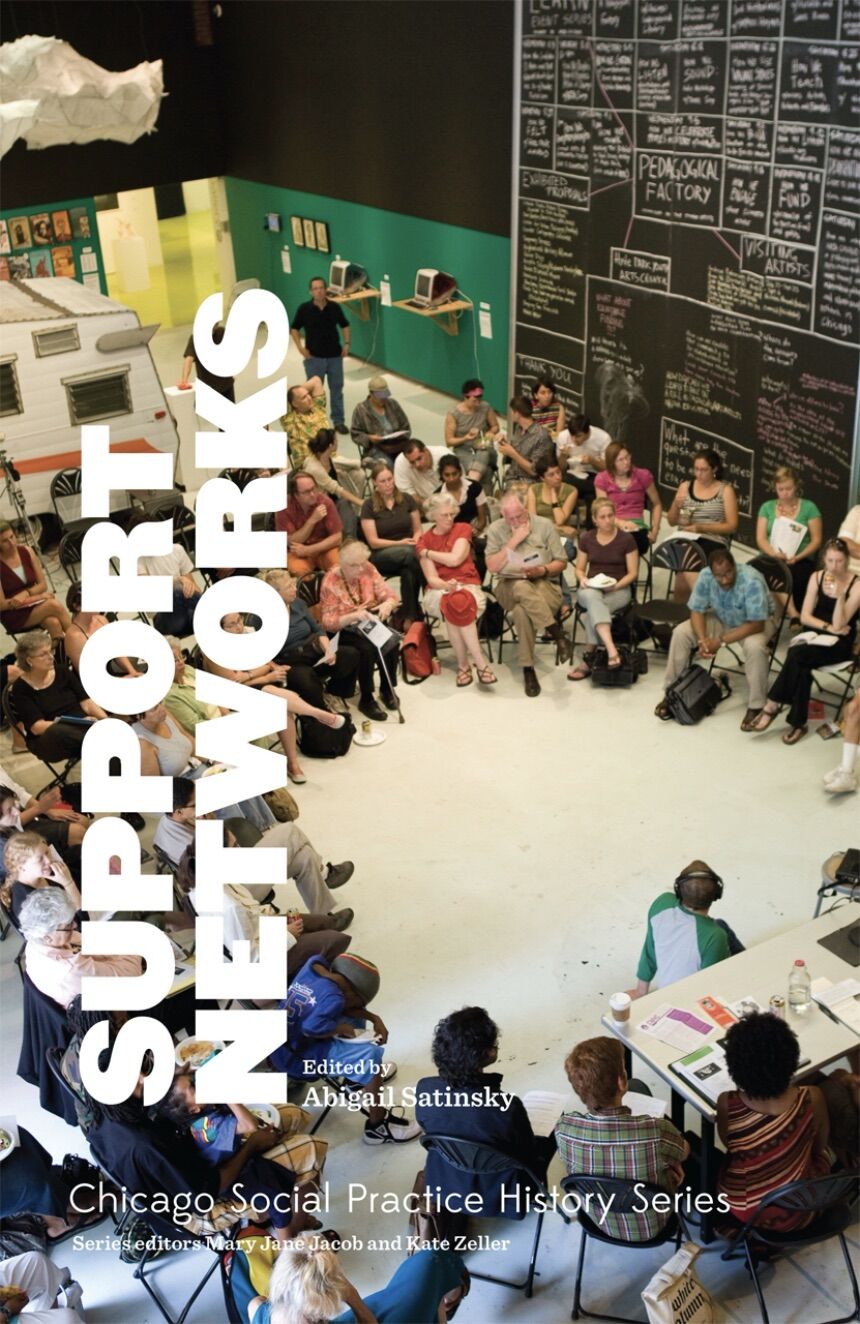 A group of people of various ages and races sit in a circle and watch a presentation