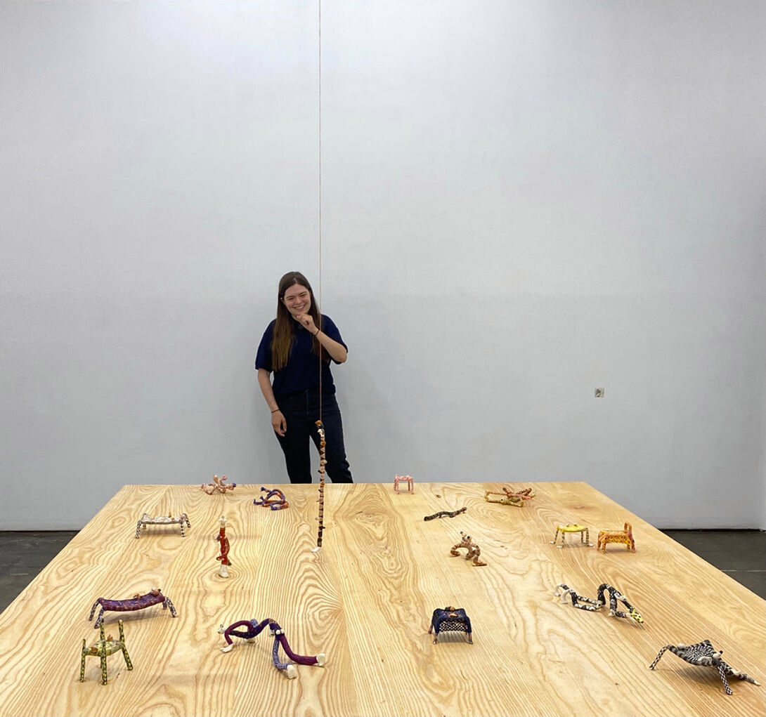 An artist stands in front of a display of small sculptures