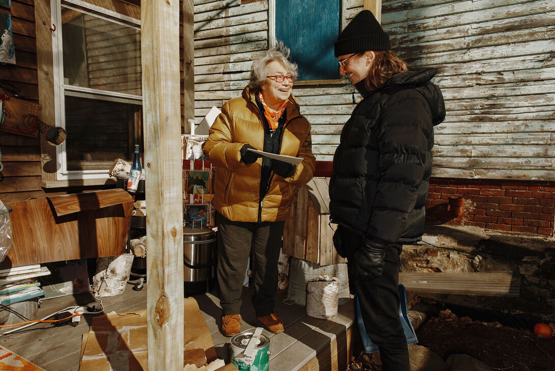 An old woman on a front porch shows a young man a folder