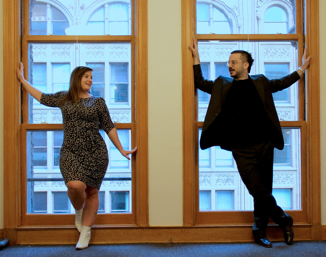 A man and a woman stand in front of a large window in a building in a city